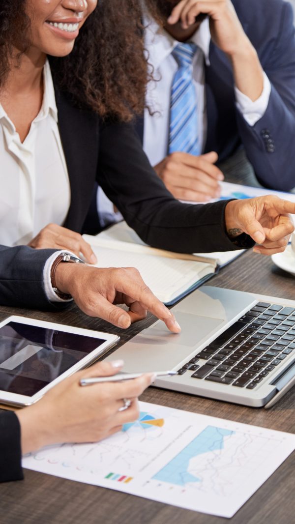 Faceless shot of coworking businesspeople surfing laptop while discussing project at table in office